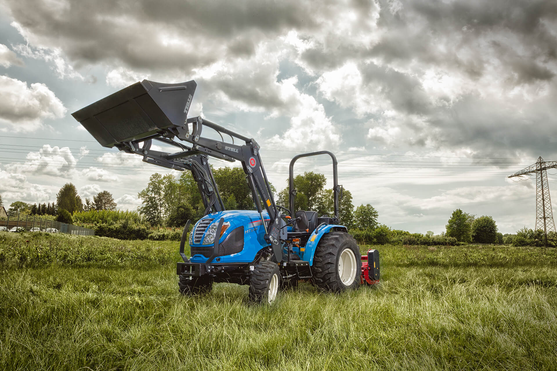 LS Kompakttraktor mit Frontlader auf einer Wiese, Schaufel angehoben